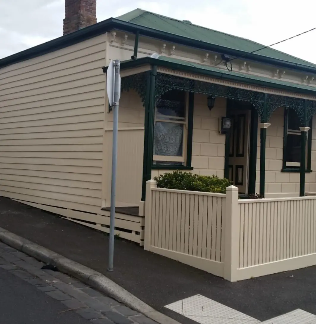 Victorian weatherboard cottage finished in cream with dark green trim, lacework and picket fence