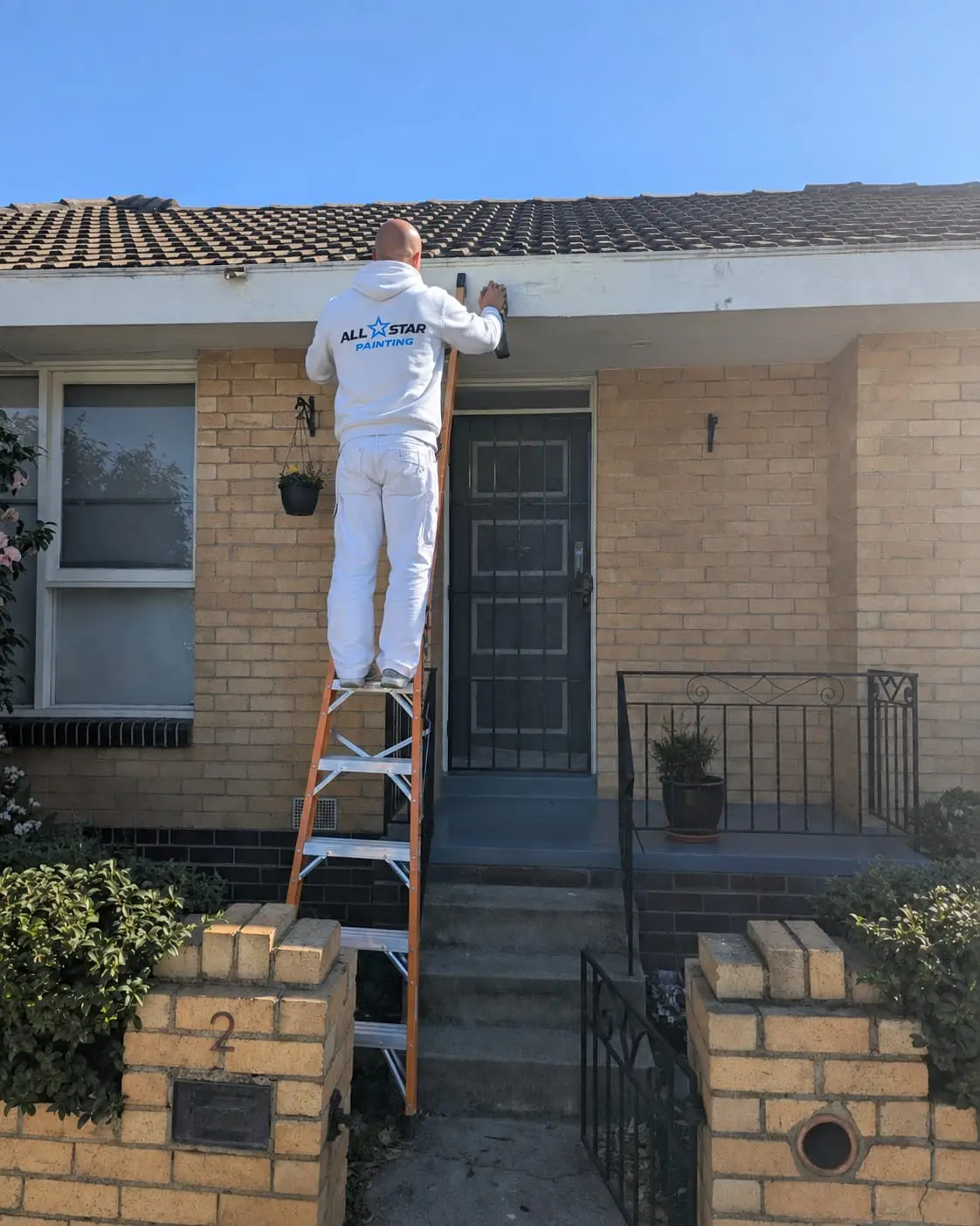 All Star painter on a ladder cutting in the fascia above a cream brick home