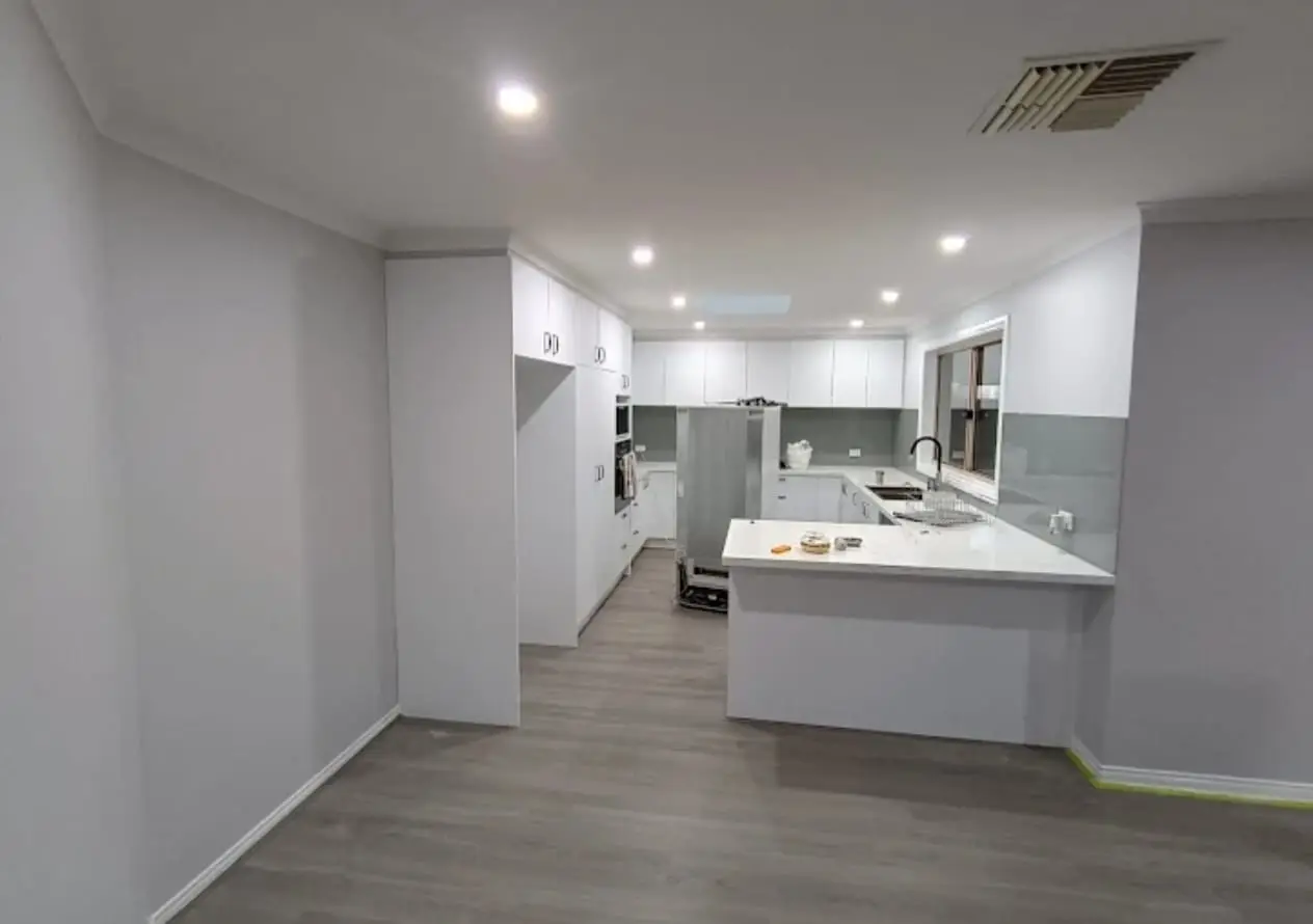 Open-plan kitchen and living room after a full repaint in soft white, tape still on the skirting
