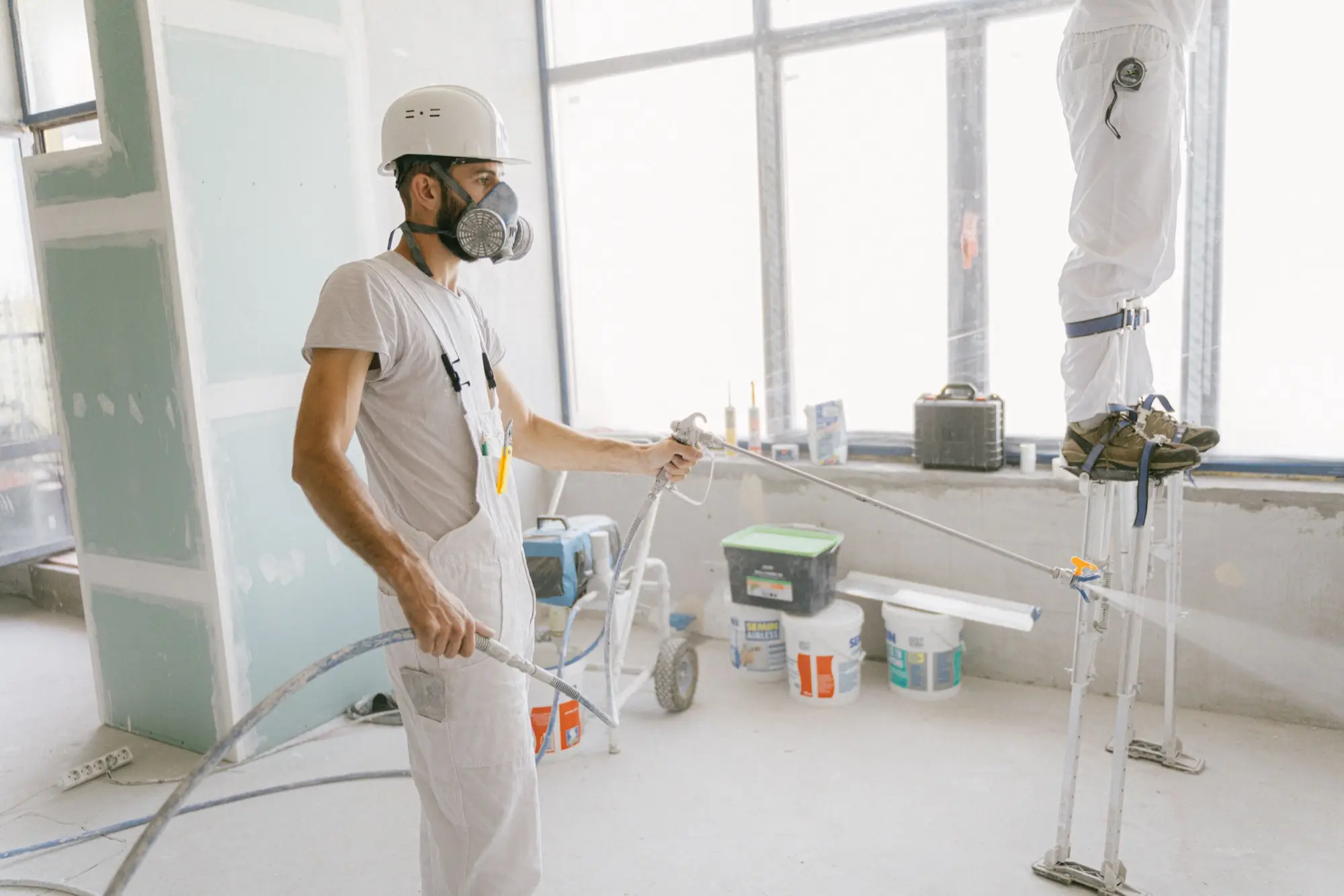 Painter in protective gear spray-painting a bright interior wall